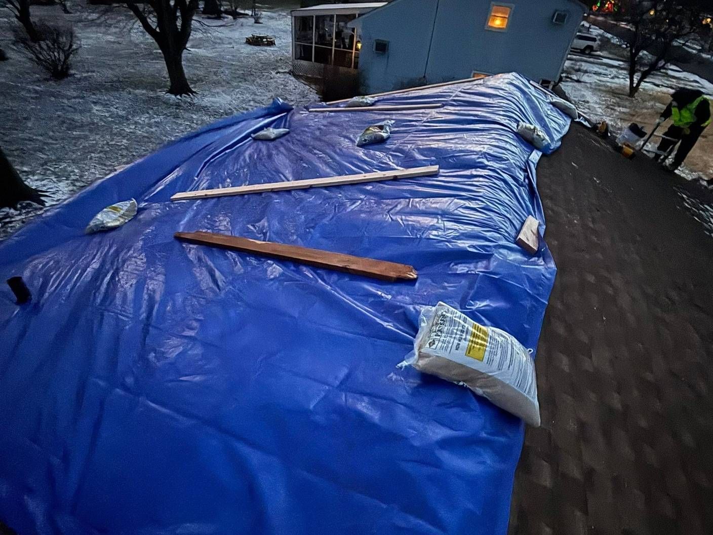 Blue emergency tarp secured on a storm-damaged roof at dusk