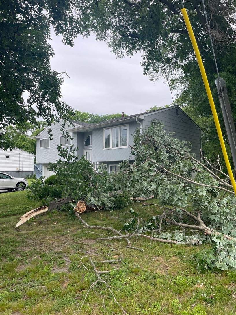 Large storm-downed tree limbs on a lawn beside a house