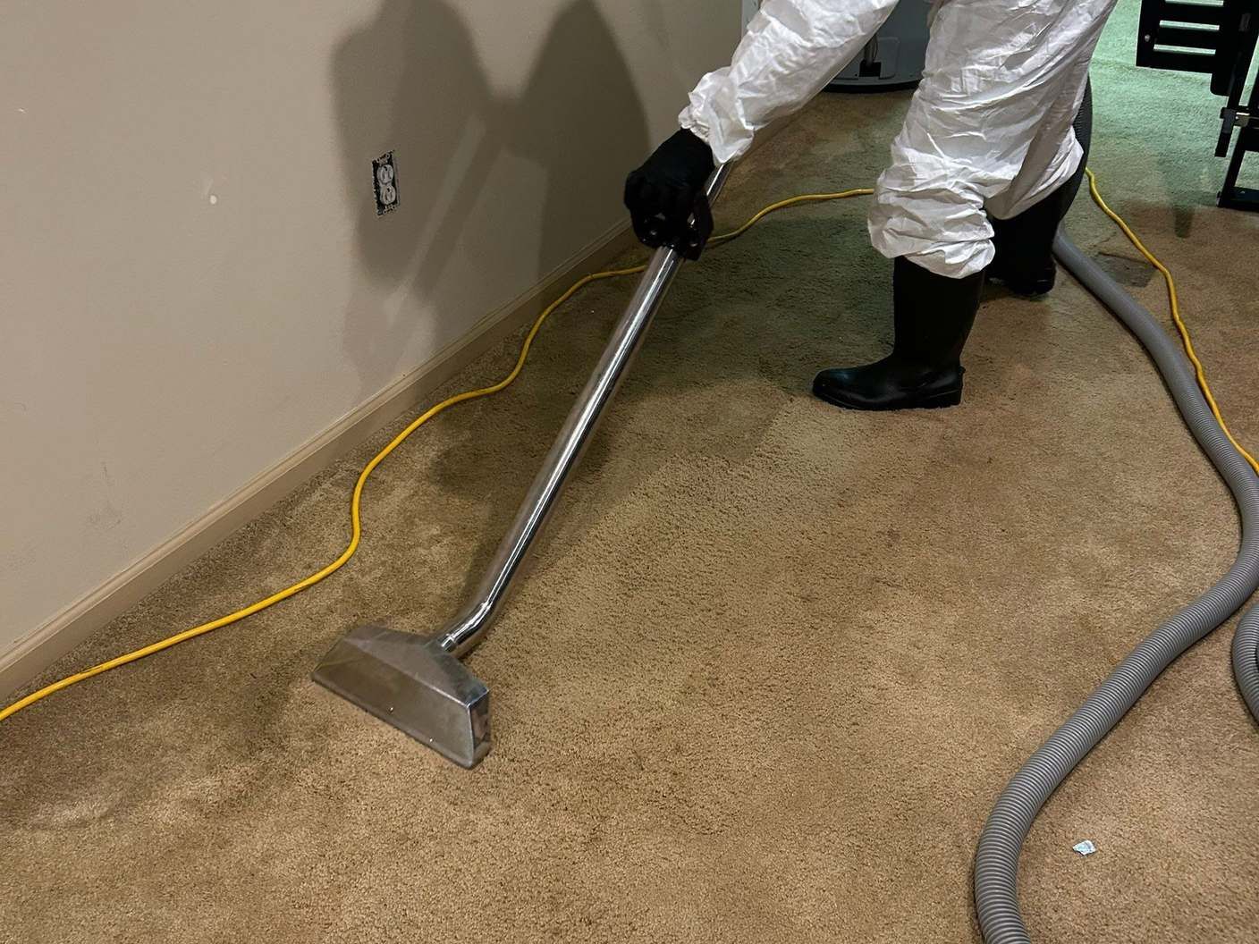 Technician in PPE extracting water from carpet with a wand