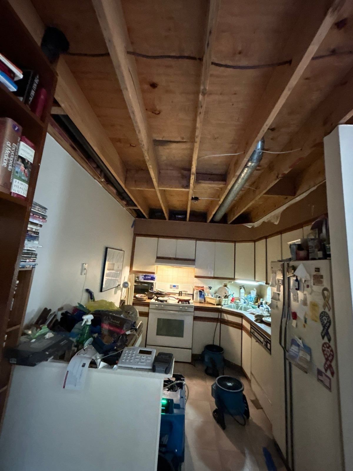 Kitchen with drywall ceiling removed to the joists and blue air movers drying the space