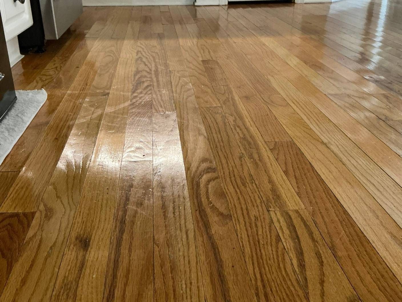 Glossy oak hardwood kitchen floor with cupped boards showing as ridges in the reflected light