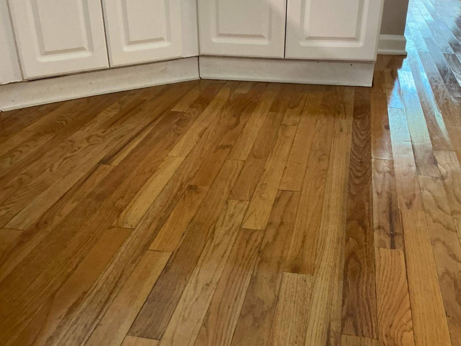 Discolored, slightly cupped oak hardwood boards in front of kitchen cabinets after water damage