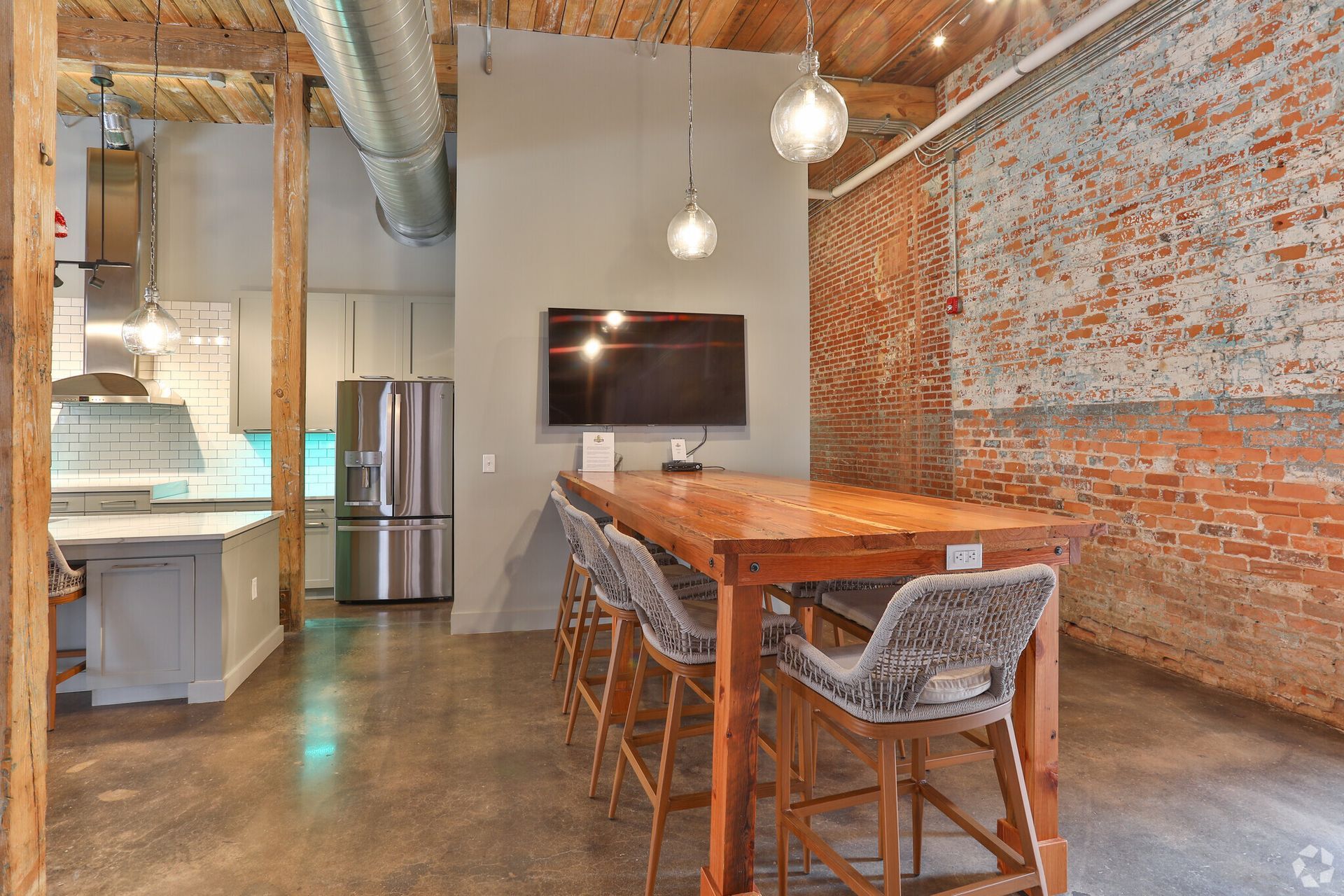 A room with a long wooden table and chairs and a flat screen tv on the wall.