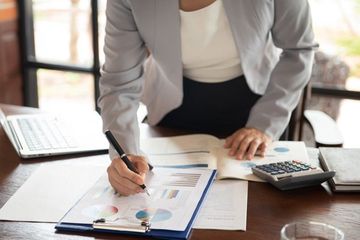 A woman is sitting at a desk writing on a clipboard.