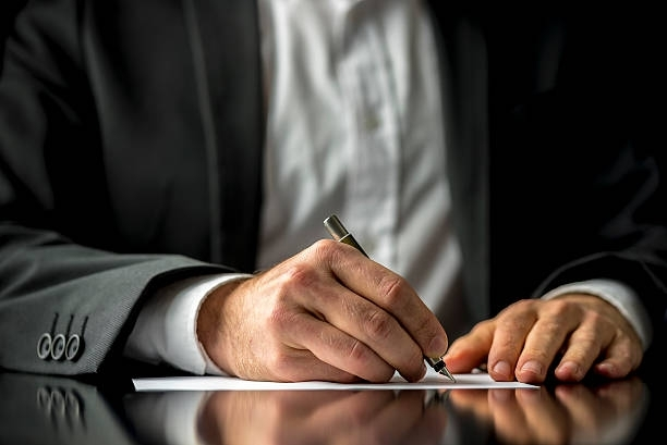 Business professional writing on paper at desk with reflection, close-up of hands and suit.
