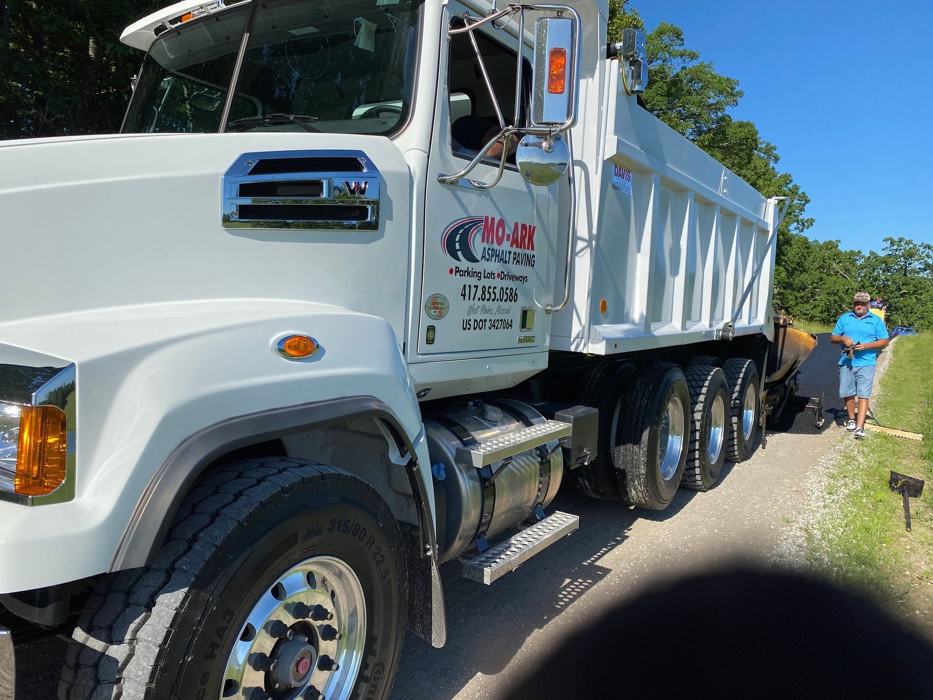 White dump truck parked roadside with a person in a blue shirt walking nearby
