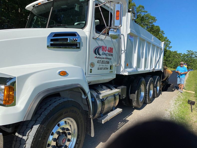 White dump truck parked on a road with a person in blue standing beside it on the right