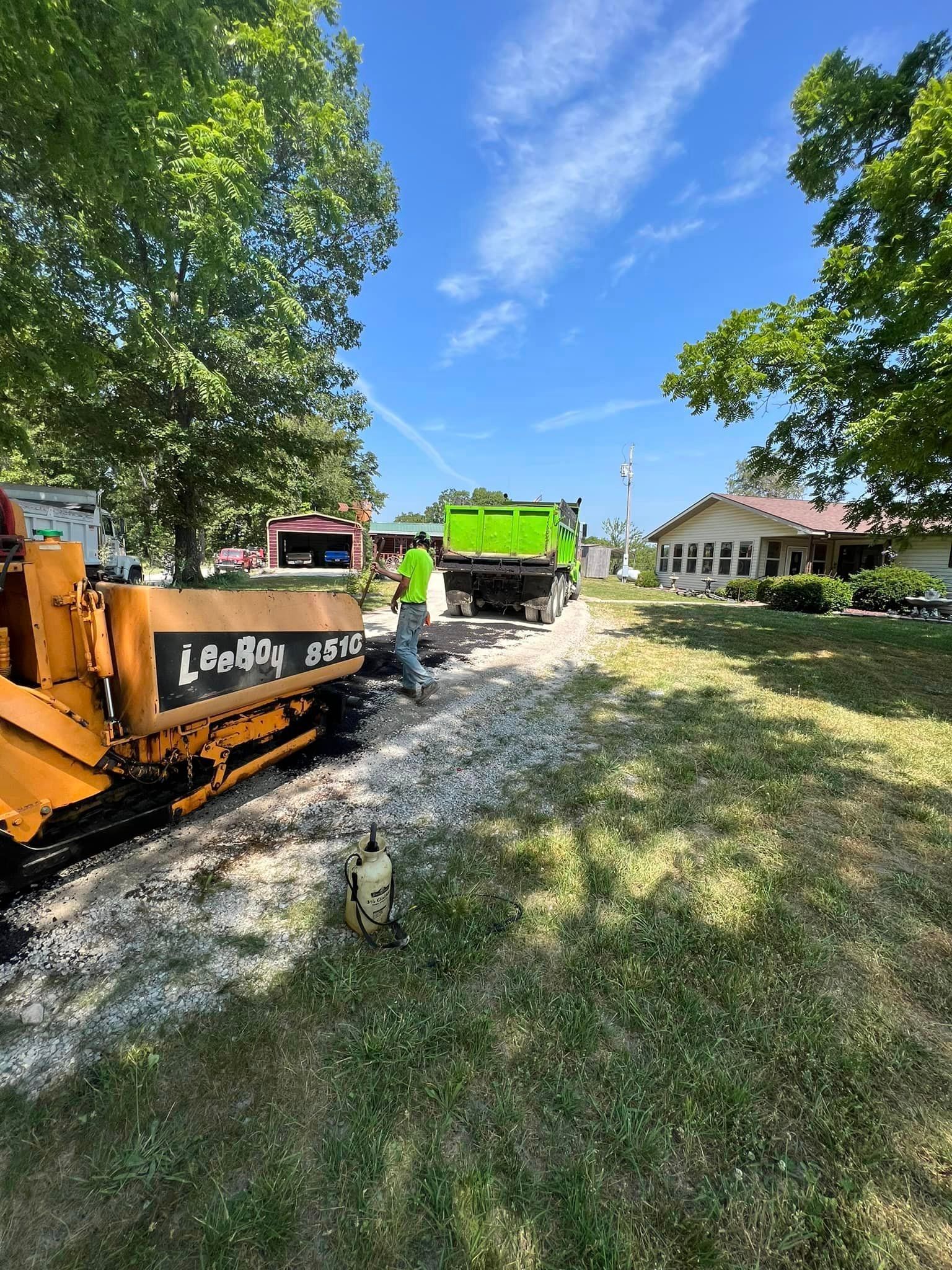 Construction equipment on a grassy residential lot with trees and a house in the background.
