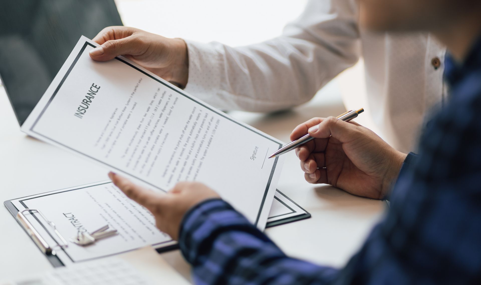 An insurance agent showing an insurance policy and pointing with a pen for the policyholder to sign.