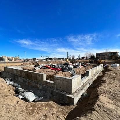 Foundation construction site with concrete walls, dirt, and materials under a bright blue sky