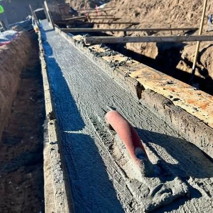 Fresh concrete walkway beside a trench, with a trowel resting on the surface at a construction site