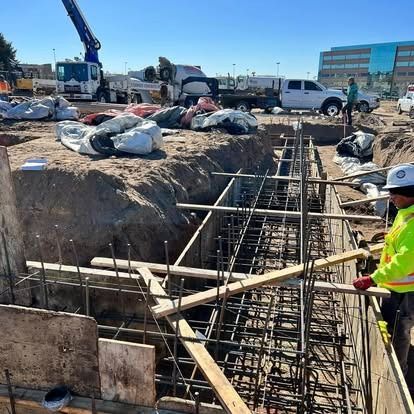 Construction worker beside rebar trench at a roadwork site, with trucks and materials in the background