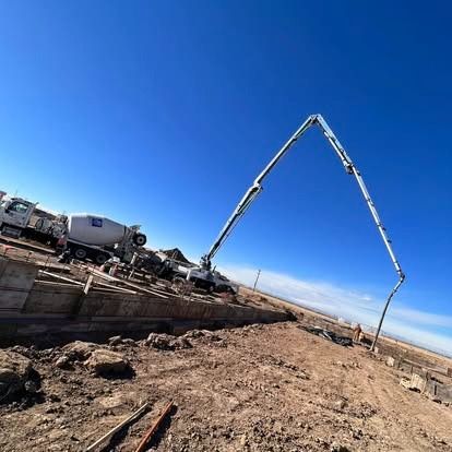 Concrete pump truck on a construction site under a clear blue sky, with a long boom extended.