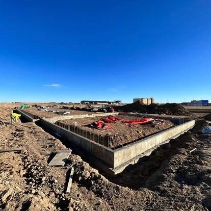 Concrete foundation under construction on a barren site, with red tarps and a bright blue sky