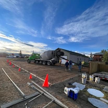 Construction site with cement mixer truck, orange cones, and workers under a blue sky