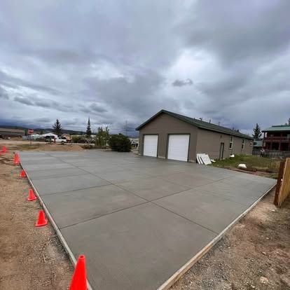 New concrete driveway beside a beige two-car garage under cloudy skies, marked with orange cones