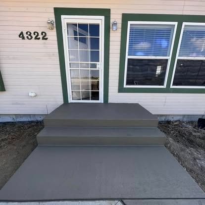 Front entry with gray steps and ramp leading to a green-trimmed door and window on a house exterior.
