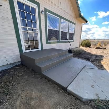 House entry with three-step concrete stoop, glass door, and large windows beside a sloped walkway.