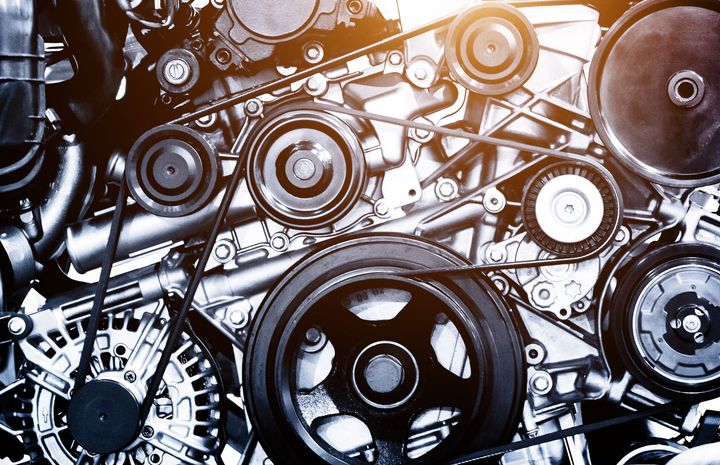 Close-up of a shiny, complex machine with gears, pulleys, and belts, likely an engine.