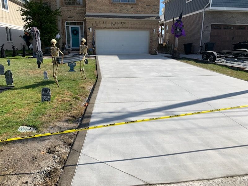 A new concrete driveway sits in front of a suburban home decorated with skeleton figures and tombstones for Halloween.