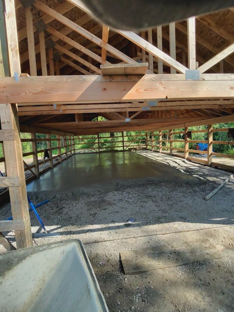 A freshly poured concrete floor inside a wooden frame building under construction, viewed from an open bay.