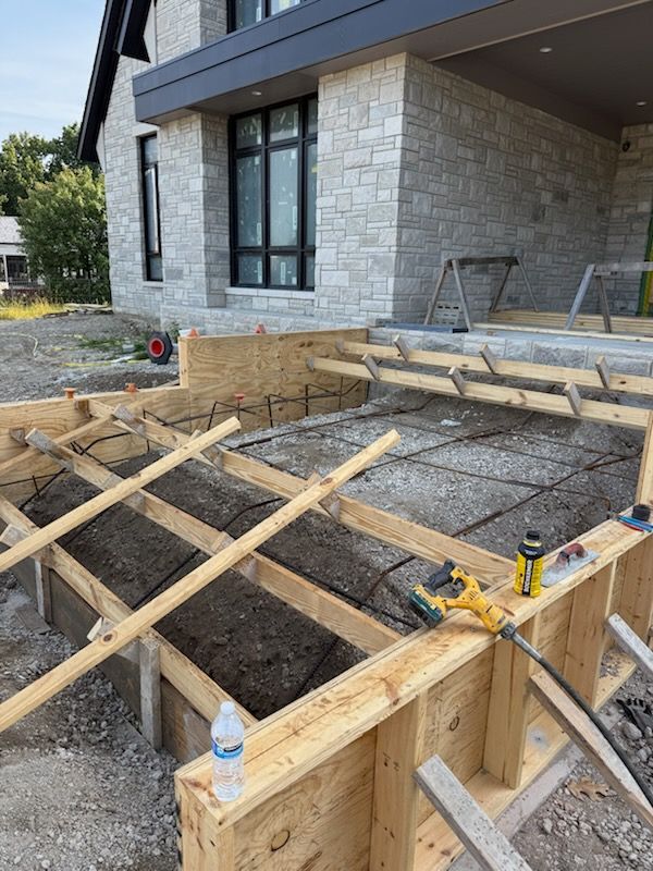 Wooden framing forms a new concrete porch or steps under construction in front of a modern stone house.