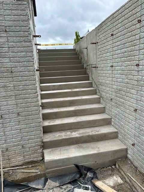 Newly constructed concrete stairs situated between two grey stone-textured walls outdoors.