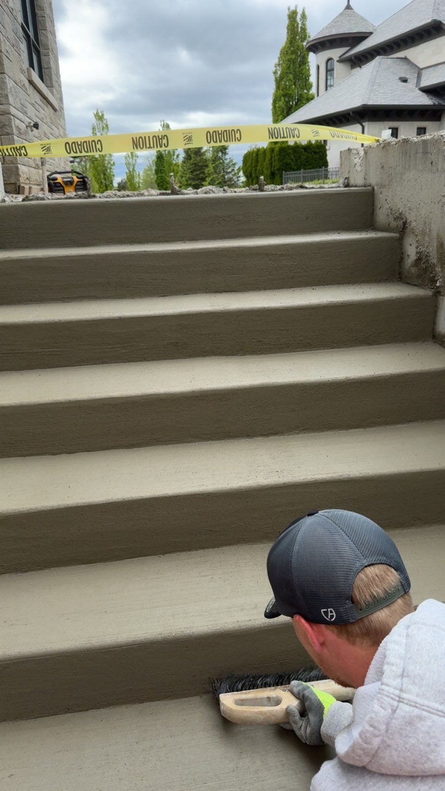 A construction worker uses a hand trowel to smooth the edge of a newly poured concrete step on a multi-level staircase.