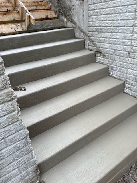 Newly poured concrete stairs leading up between two textured stone walls, with wooden forms visible at the top.