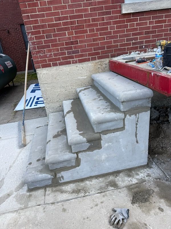 Newly installed concrete steps leading up to a red entryway, showing visible mortar and finishing work in progress.