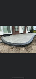 A curved concrete patio with a dark border installed outside the back of a brick house.