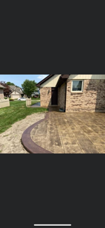 A newly installed stamped concrete patio with a dark, rounded border next to a brick house and grassy backyard.