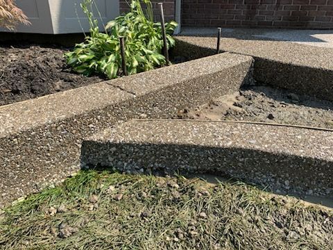 Exposed aggregate concrete steps transition to dirt, with thin metal stakes protruding from the ground nearby.
