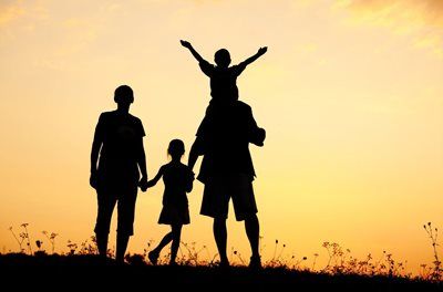 Silhouetted family of three holding hands on a hill at sunset