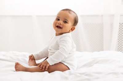 Smiling baby sitting on a white bed in a bright room