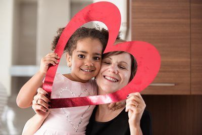 Smiling child and adult holding a red heart frame in a kitchen