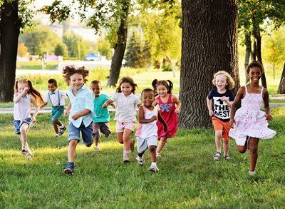 Children running and smiling through a sunny park with trees and grass