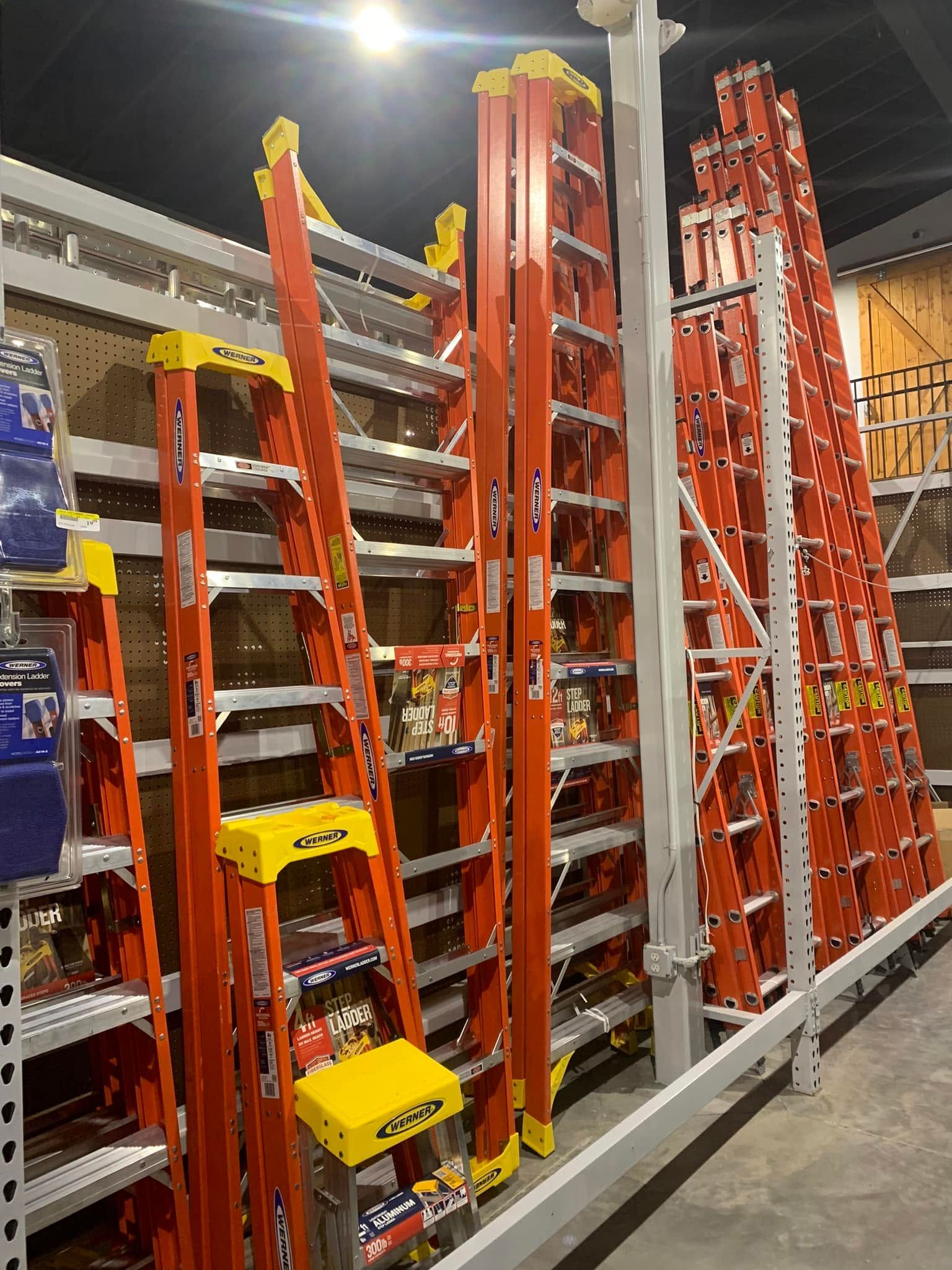 Stacked ladders and scaffolding leaning in a hardware store aisle, mostly orange and gray.