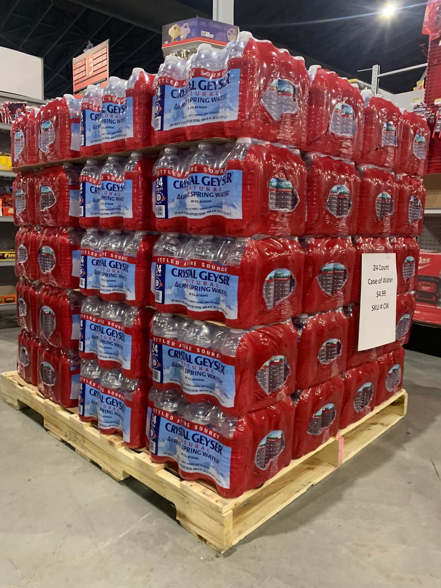 Pallet stack of red bottled water cases wrapped in plastic on a warehouse floor