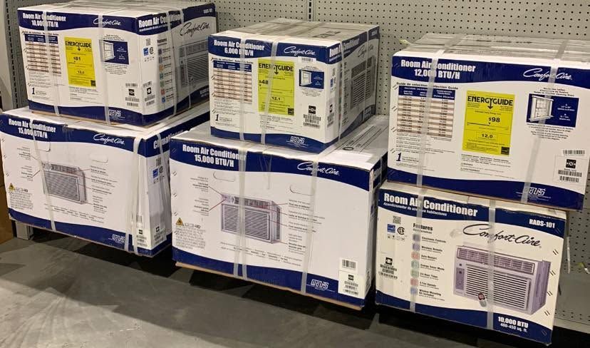 Stacks of white and blue shipping boxes with labels, piled on pallets in a warehouse aisle.