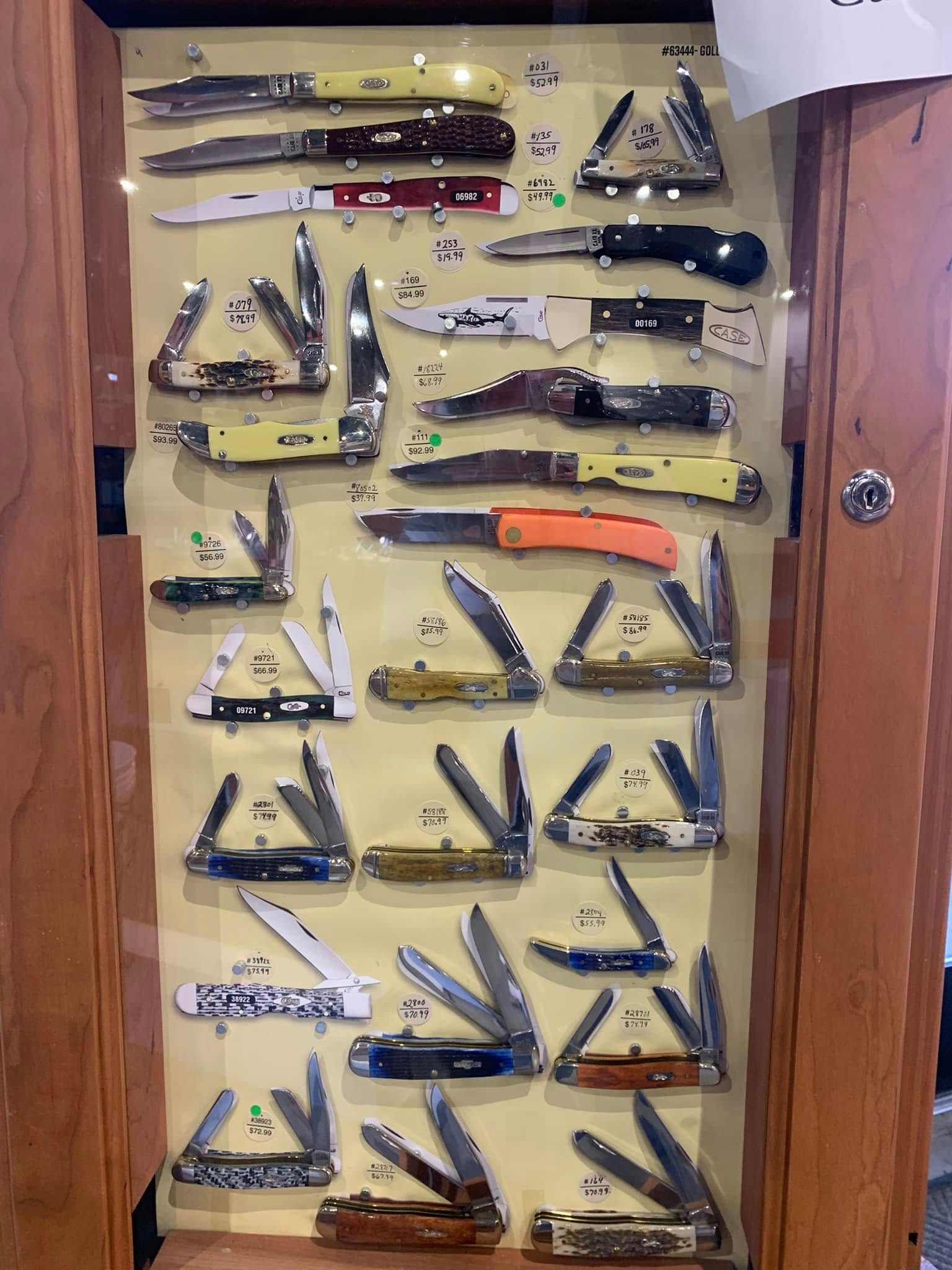 Knife collection displayed in rows behind a glass cabinet door, with one orange-handled knife in the center