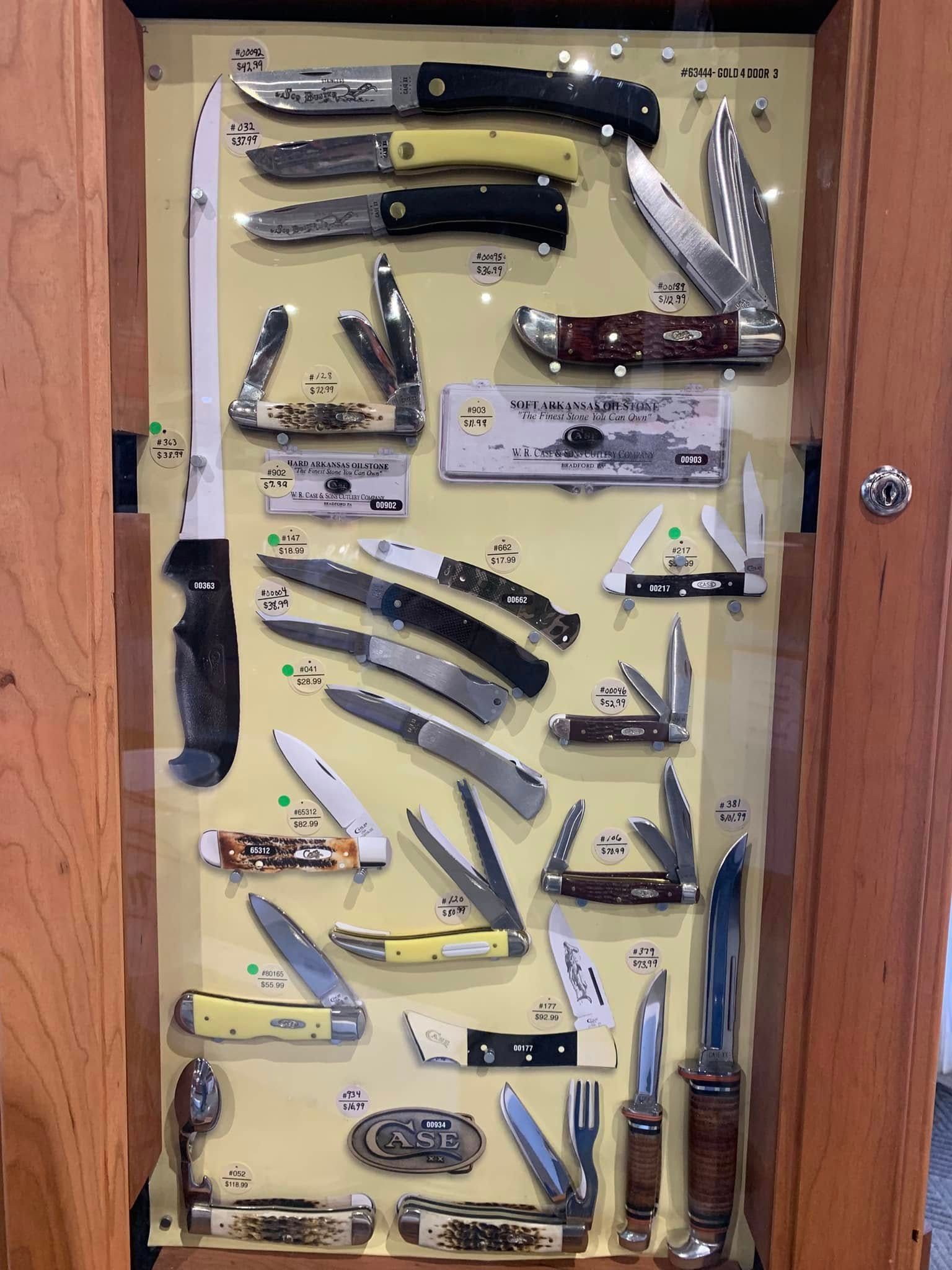 Assorted folding knives displayed on a wooden board, arranged in rows with various handles and blades.