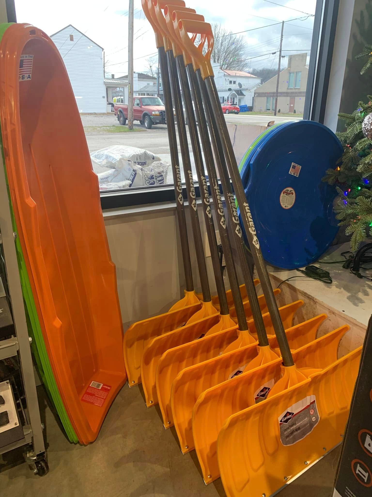 Orange folding chairs stacked in a store window beside a large orange surfboard and blue circular object