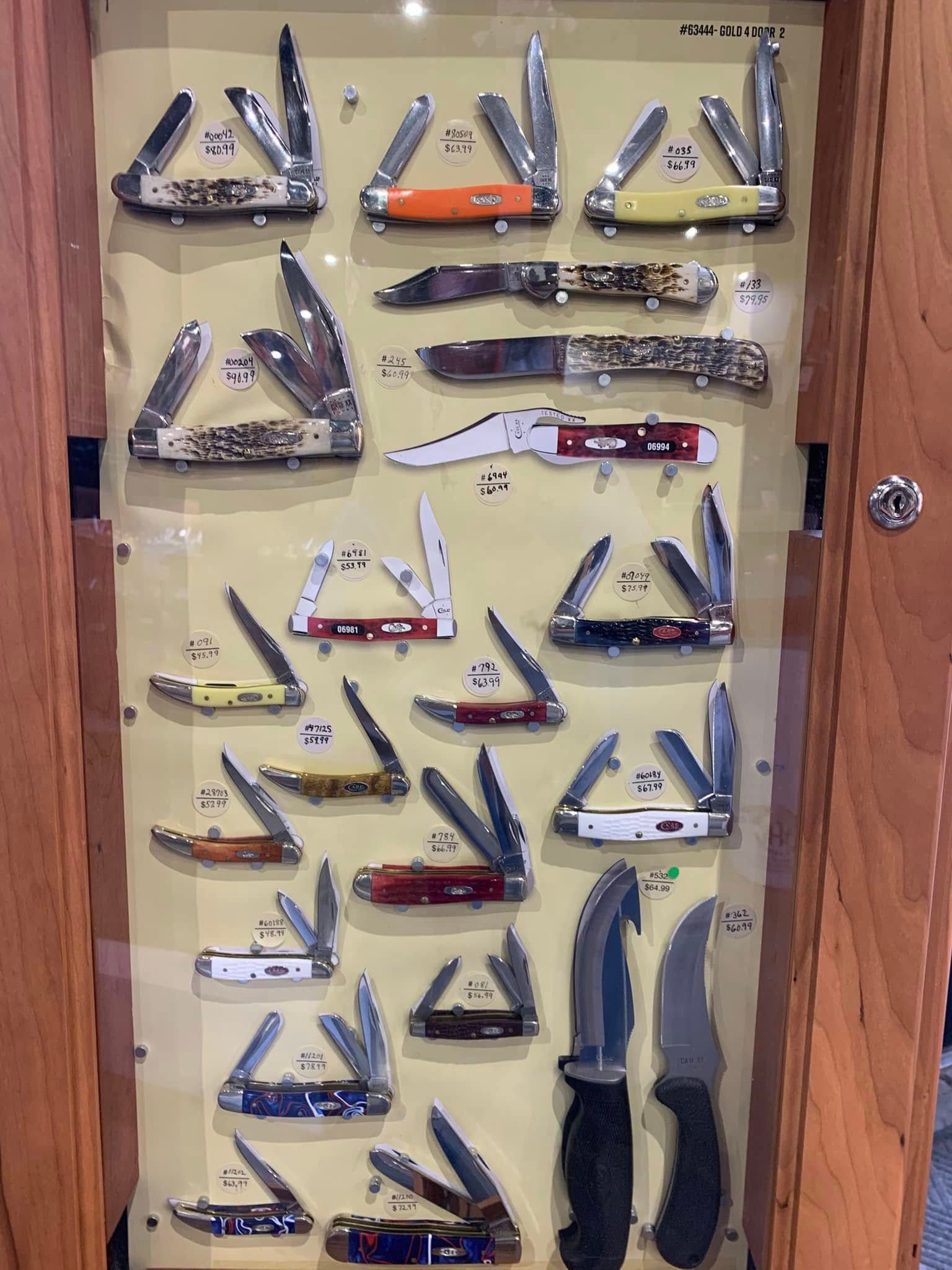 Assorted folding knives and pocketknives displayed in a glass-front wooden case.