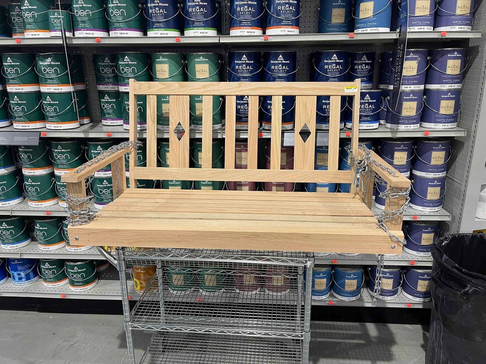 Wooden bench display in a store aisle, with rows of paint cans on shelves behind it.