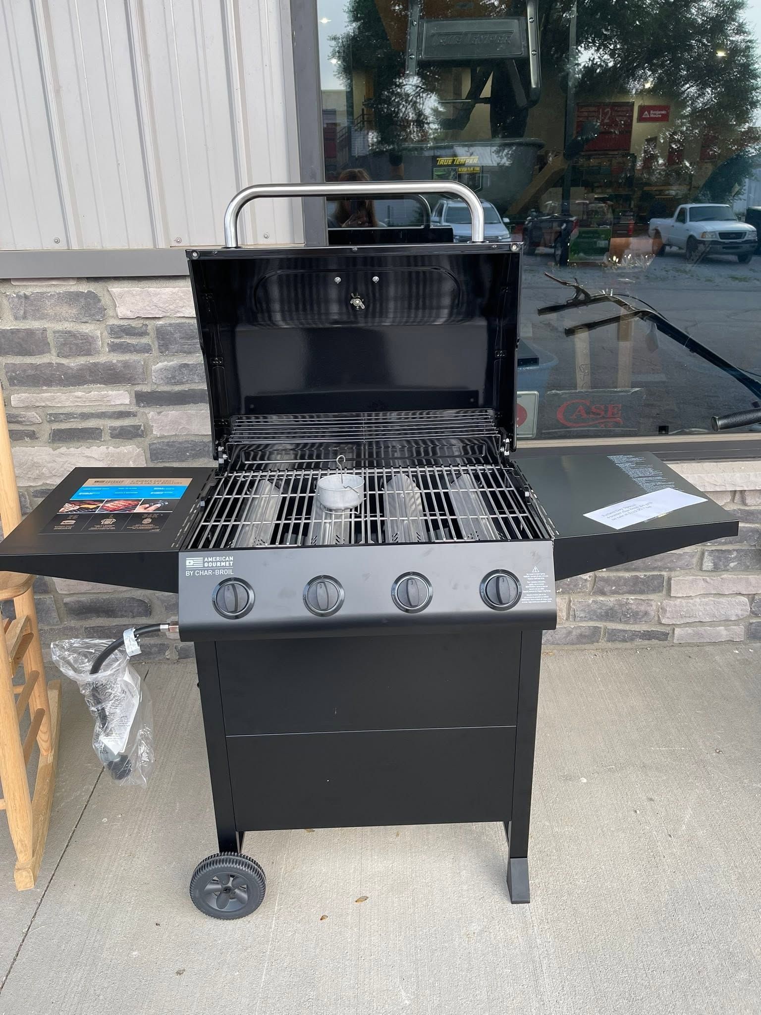 Black gas grill with lid open and side shelves, shown outdoors on a patio.