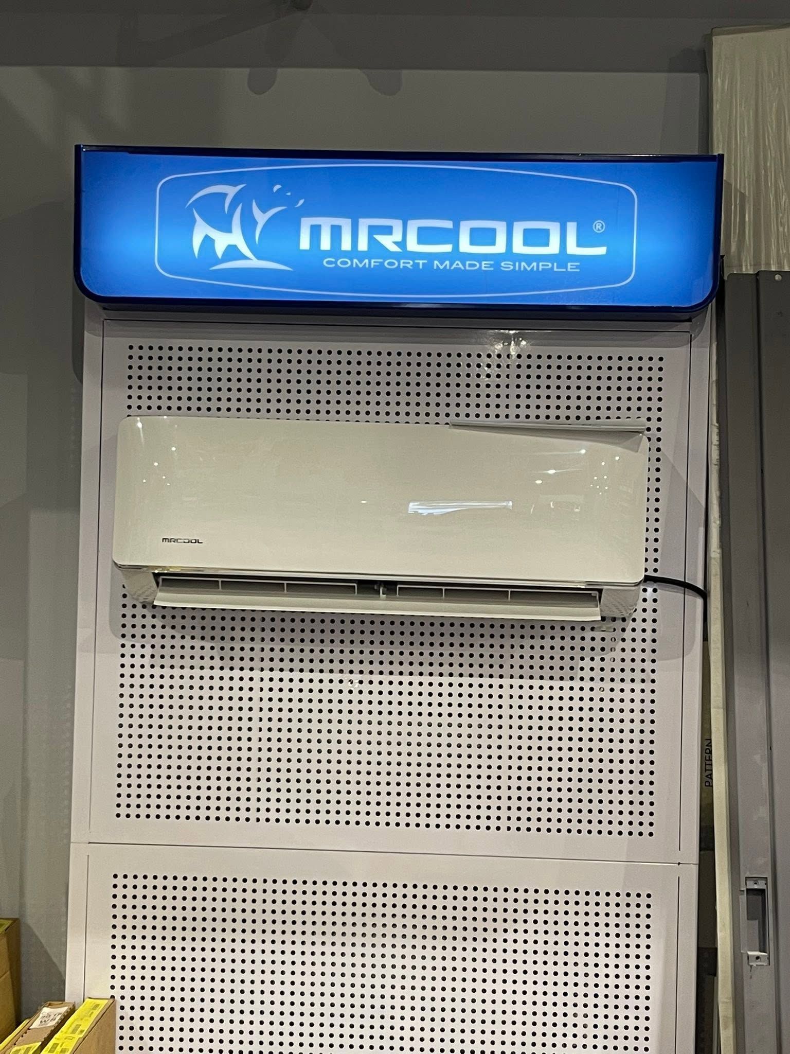 Blue MrCool wall-mounted air conditioner on a perforated metal panel indoors