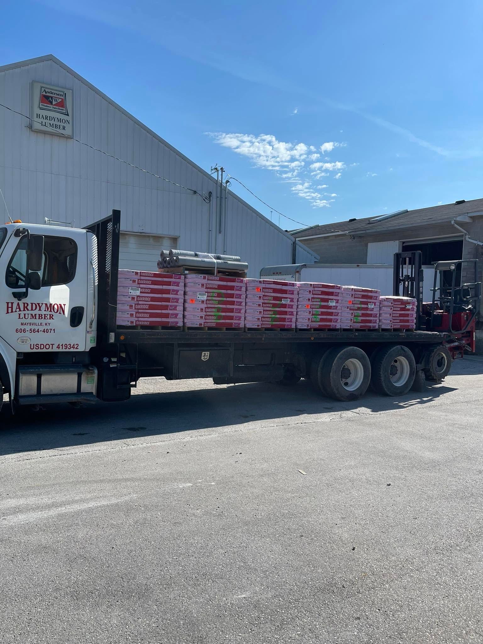 Flatbed truck loaded with pink bagged materials parked beside a warehouse in bright sunlight