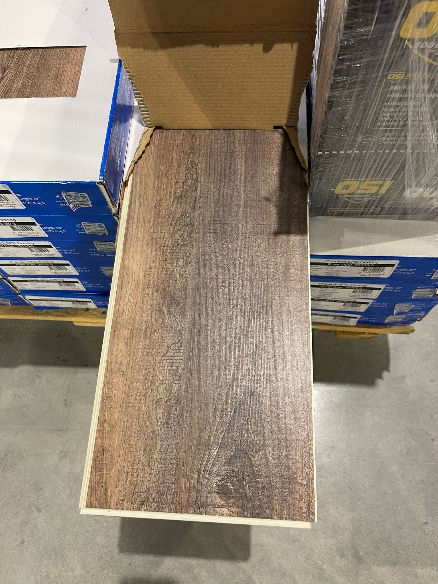 Open cardboard box with a wood-patterned panel ramp extending onto a warehouse floor.