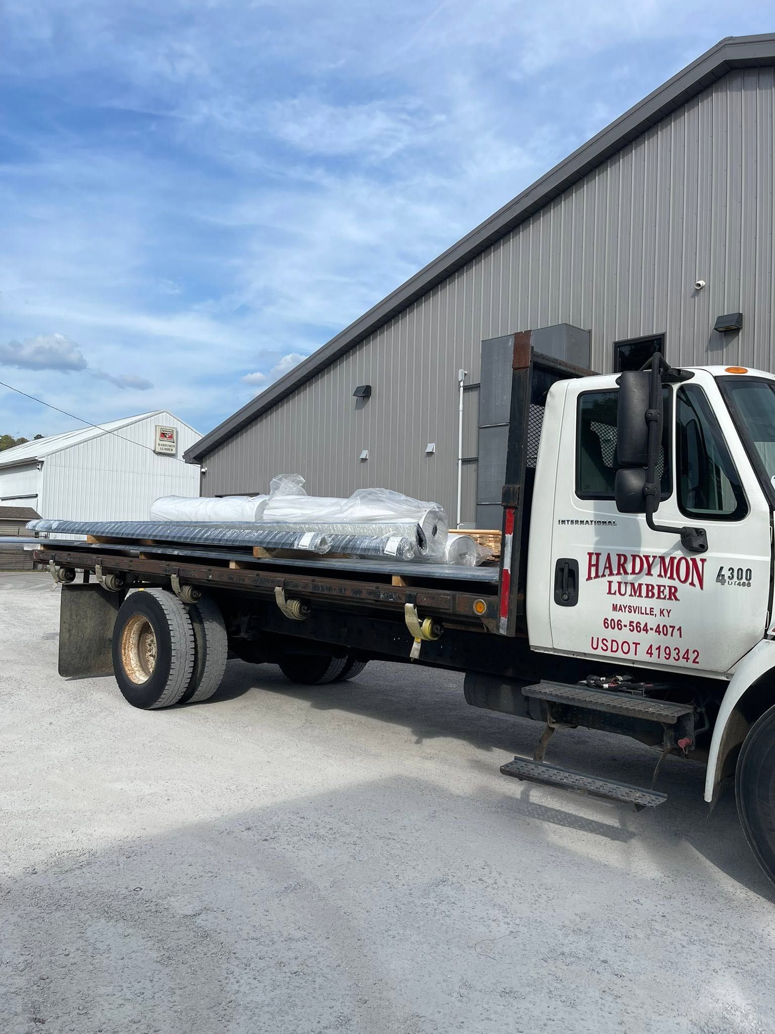 Flatbed tow truck loaded with wrapped debris parked beside a gray industrial building.